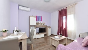 A modern hotel room with a wooden floor, a bed with a pink and white striped bedspread, a desk with a chair, a television, and a small table with a bottle of champagne. - Villa Nea Zadarvillas (Posedarje)
