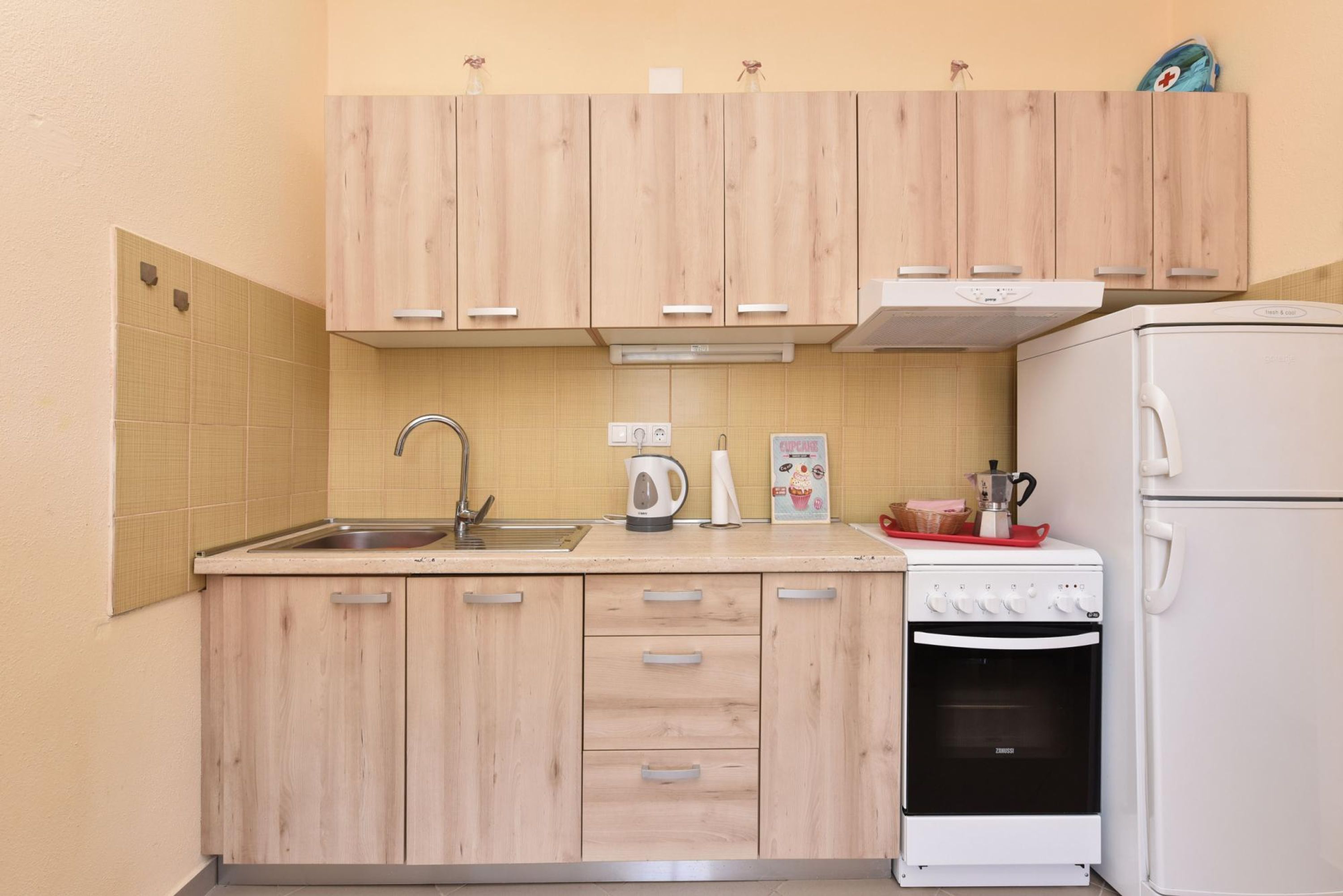A compact kitchen with wooden cabinets, a sink, a stove, and a refrigerator.