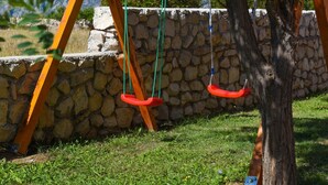 A stone wall, a swing set, and a grassy area with a tree. - Villa Nea Zadarvillas (Posedarje)