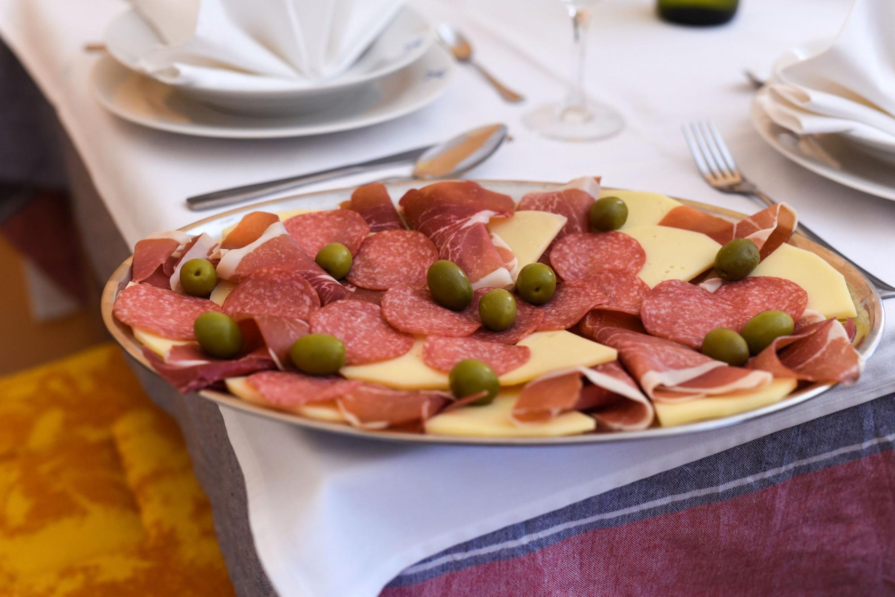 A platter of assorted meats and cheese, olives, and a wine glass on a table.