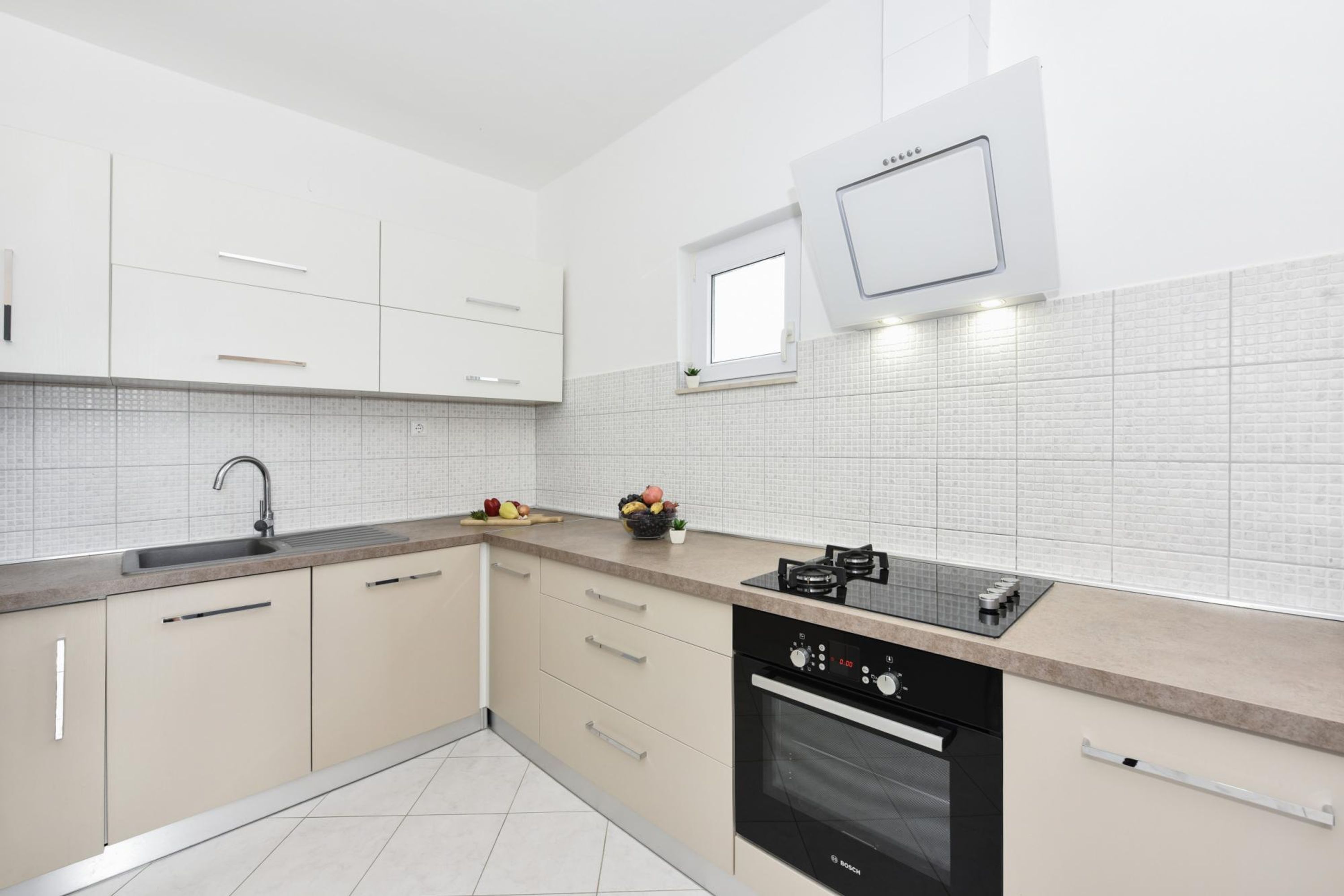 Una cocina moderna con armarios blancos, horno empotrado y encimera con fregadero y cocina.