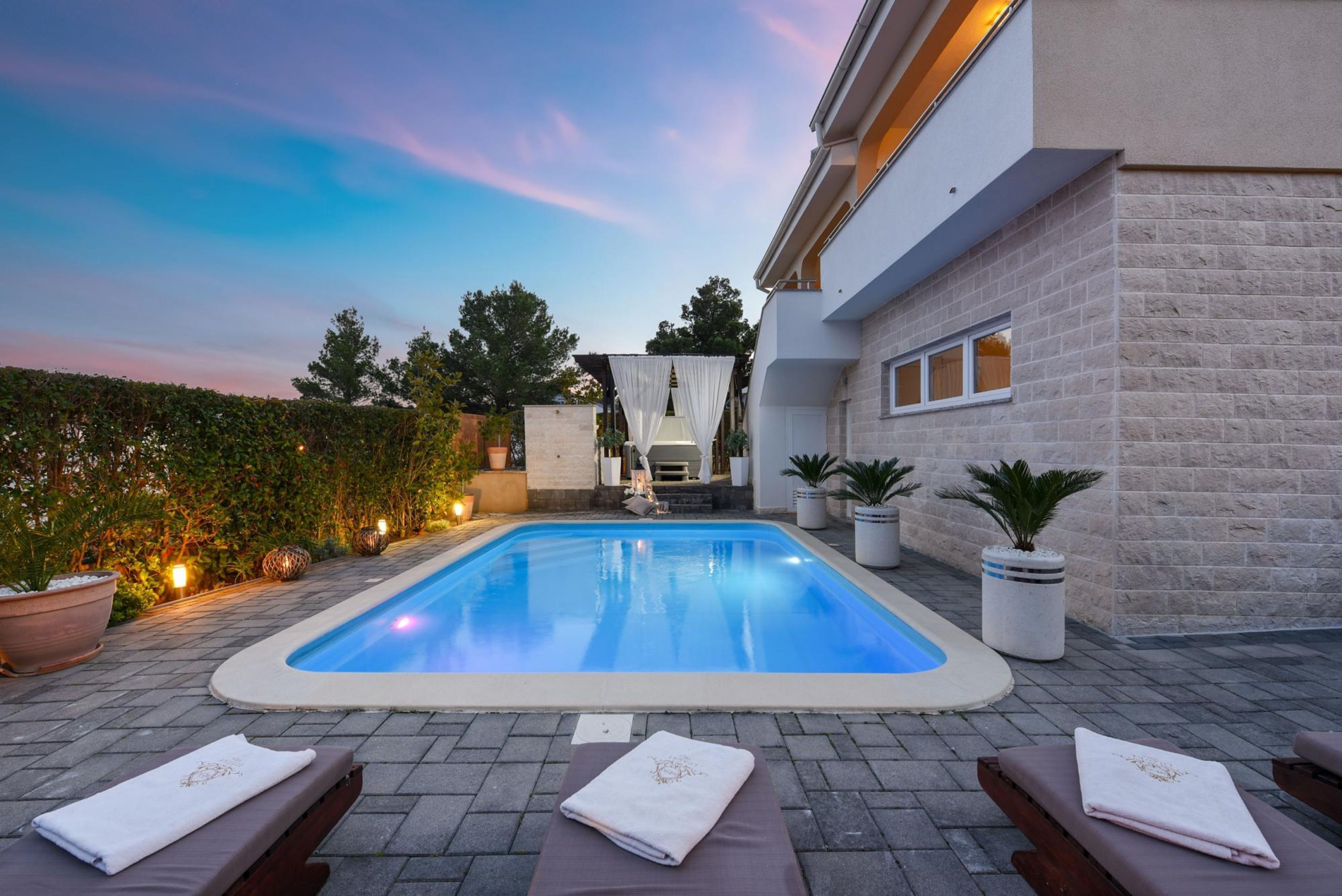 A swimming pool with lounge chairs and towels, surrounded by potted plants and a hedge.