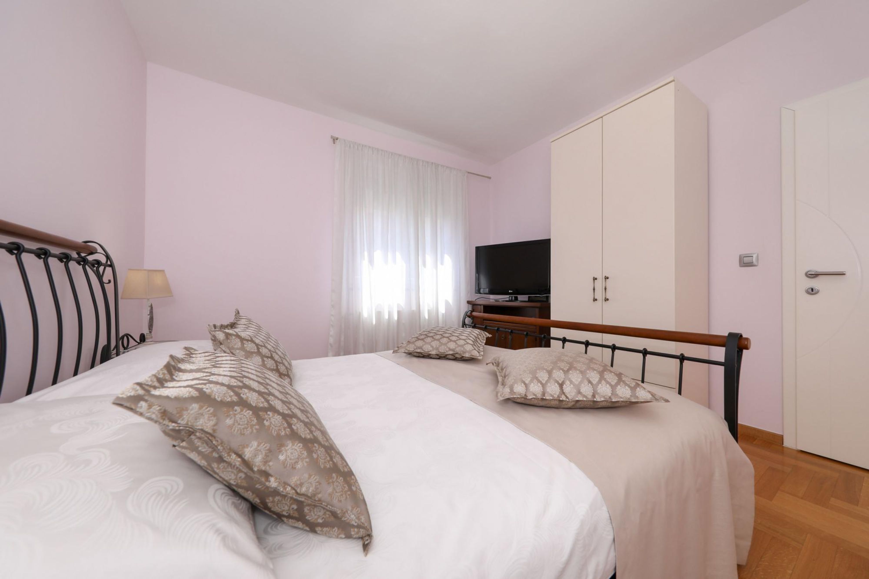 Ein Schlafzimmer mit zwei Betten, einem Kleiderschrank, einem Fernseher und einem Fenster mit Vorhängen.