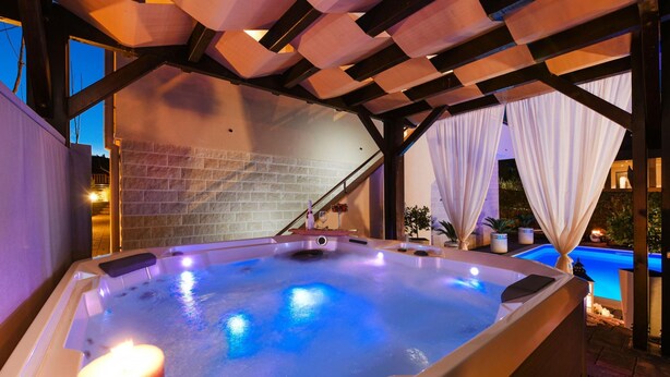 A hot tub under a wooden pergola with a brick wall backdrop and a pool in the background. - Villa Bella Zadarvillas (Novigrad)