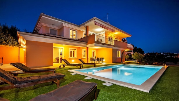 Une maison à deux étages avec une piscine, un espace salon extérieur et un balcon bien éclairé.