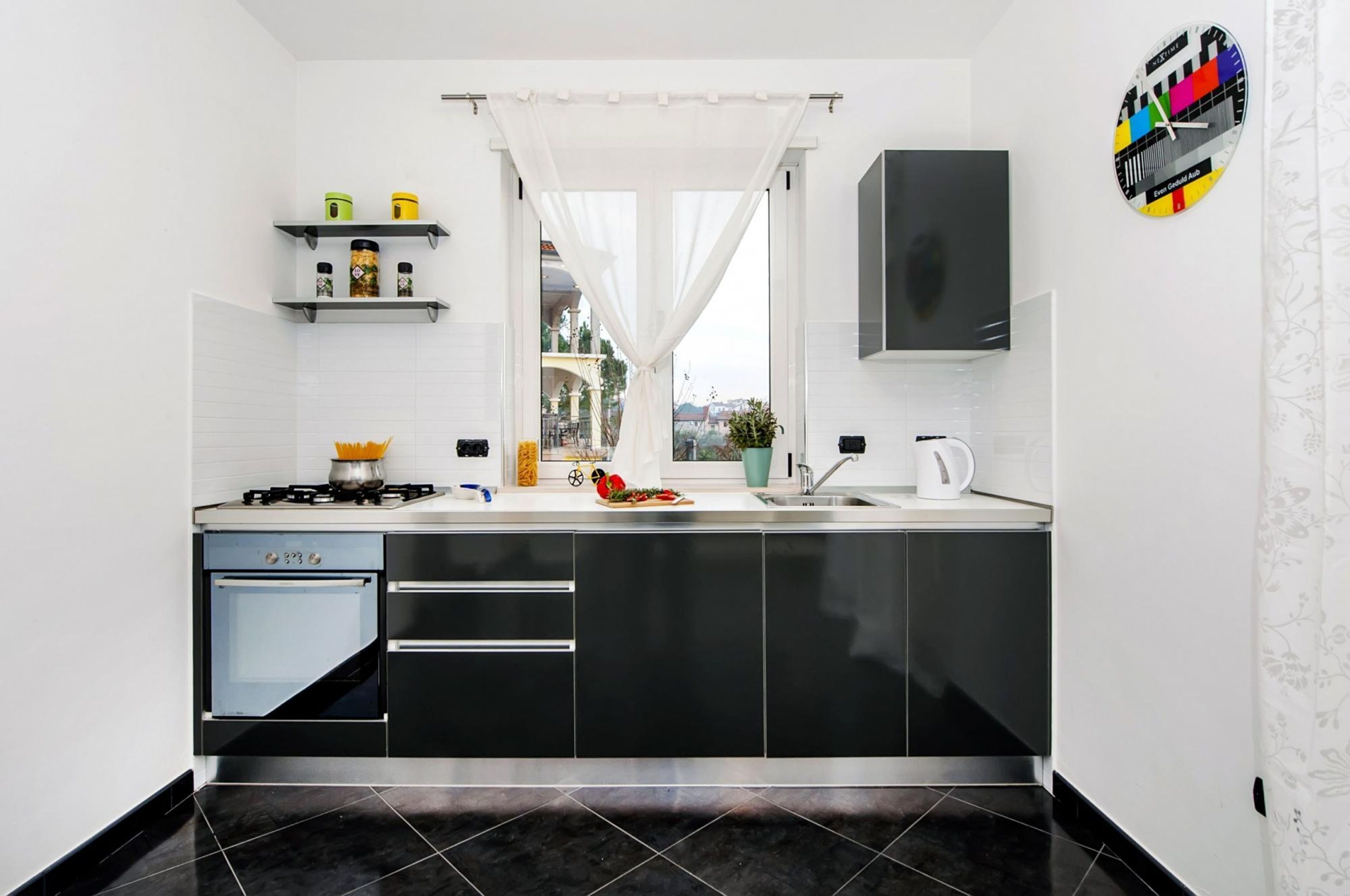 A modern kitchen with black cabinets, a gas stove, a sink, and a window with white curtains.