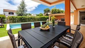 Un espace extérieur abrité, aménagé pour les repas, avec une piscine, des meubles en osier et un panier de fruits.