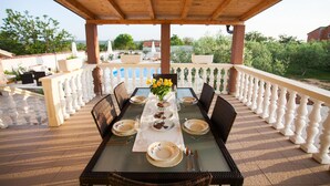 An outdoor dining area with a wooden pergola, white balustrade, and a table set for four with plates, glasses, and a vase of yellow flowers. - Villa Olive Zadarvillas (Policnik)