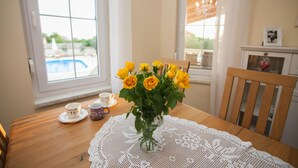 A wooden dining table with a lace tablecloth, a clear glass vase with yellow roses, and two cups on saucers. - Villa Olive Zadarvillas (Policnik)