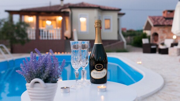 A bottle of Prosecco and two glasses on a white table by a pool, with a house in the background. - Villa Olive Zadarvillas (Policnik)
