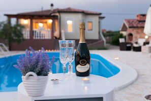 A bottle of Prosecco and two glasses on a white table by a pool, with a house in the background. - Villa Olive Zadarvillas (Policnik)