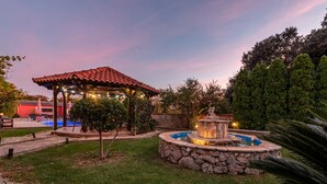 Un pabellón con una fuente de piedra, una piscina y un jardín bien cuidado.