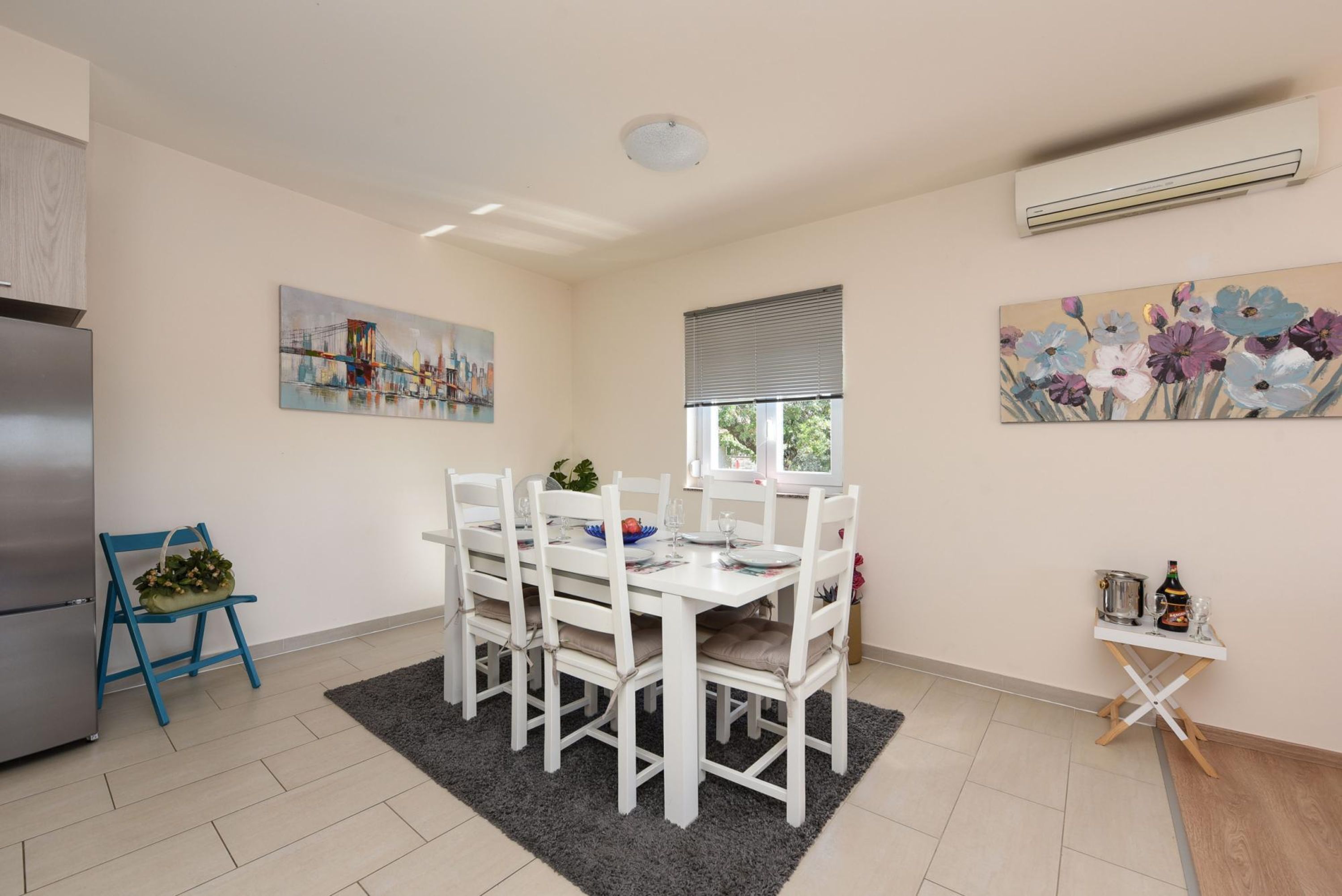 Une cuisine moderne avec des meubles blancs, une table à manger pour quatre personnes et des œuvres d’art accrochées aux murs.