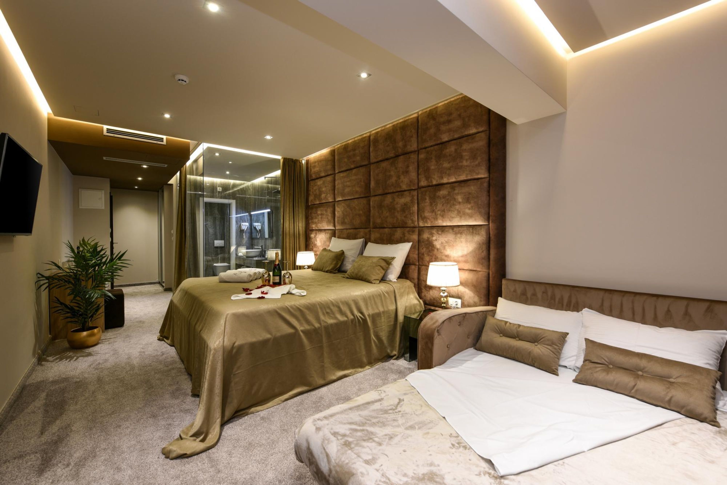 A modern hotel room with a large bed, a smaller bed, a seating area, and a TV mounted on the wall.