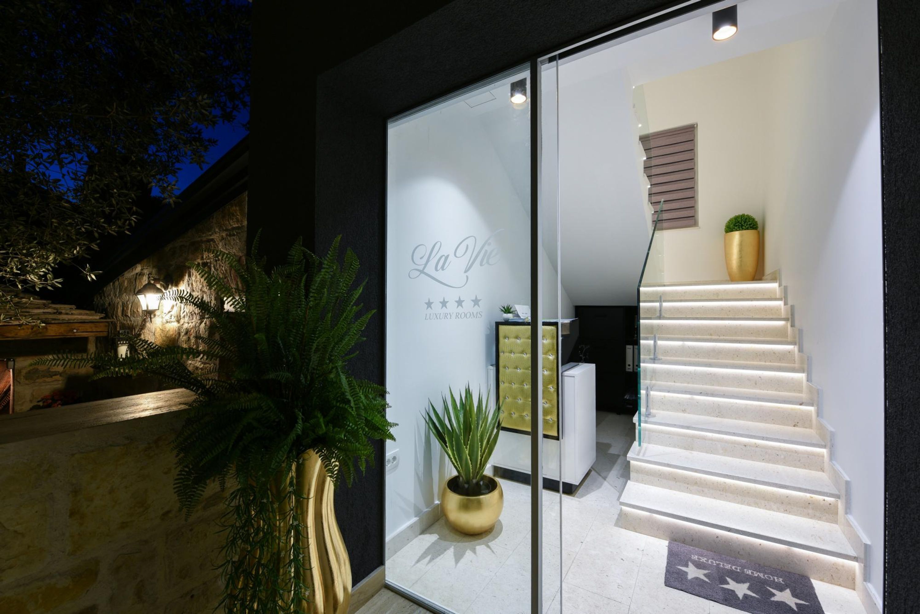 Entrada moderna de un hotel con puerta de vidrio, escalera y un cartel que dice "La Vie Luxury Rooms".