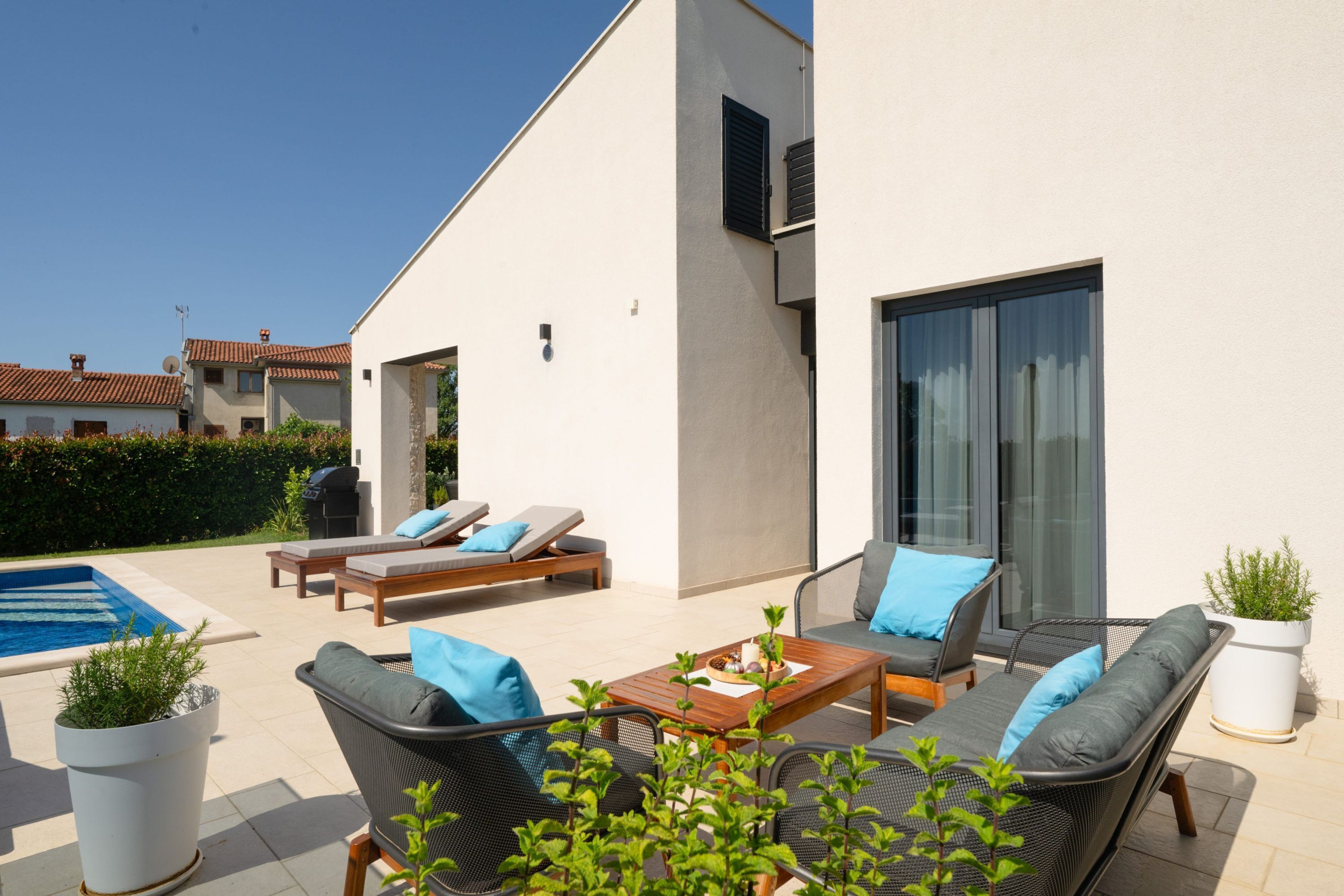 A modern outdoor patio with lounge chairs, a wooden table, and potted plants.