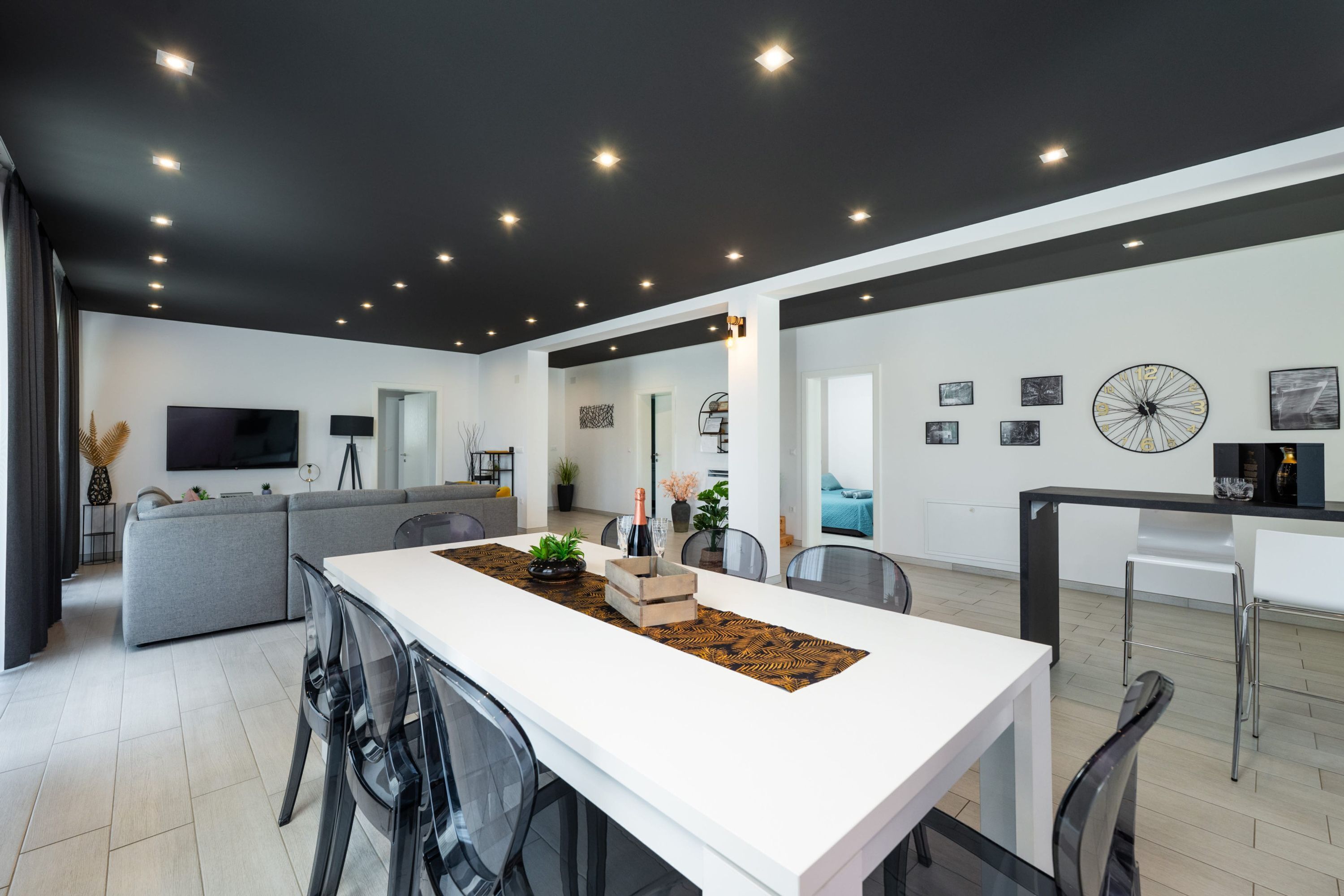 Un salon moderne avec un canapé blanc, un coin repas doté d’une longue table et une cuisine en arrière-plan.