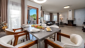 A dining area with a table set for four, surrounded by chairs, with a view of the outdoors through large windows. - Villa Antea Zadarvillas (Zadar)