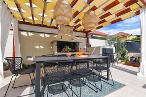 Eine Terrasse im Freien mit Tisch, Stühlen, Grill und hängenden Lichtern.