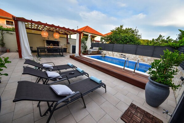 An outdoor patio with lounge chairs, a barbecue area, and a swimming pool.