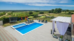 Ein Schwimmbecken mit Blick auf die Landschaft, ein Spielbereich für Kinder und Sitzmöglichkeiten im Freien.