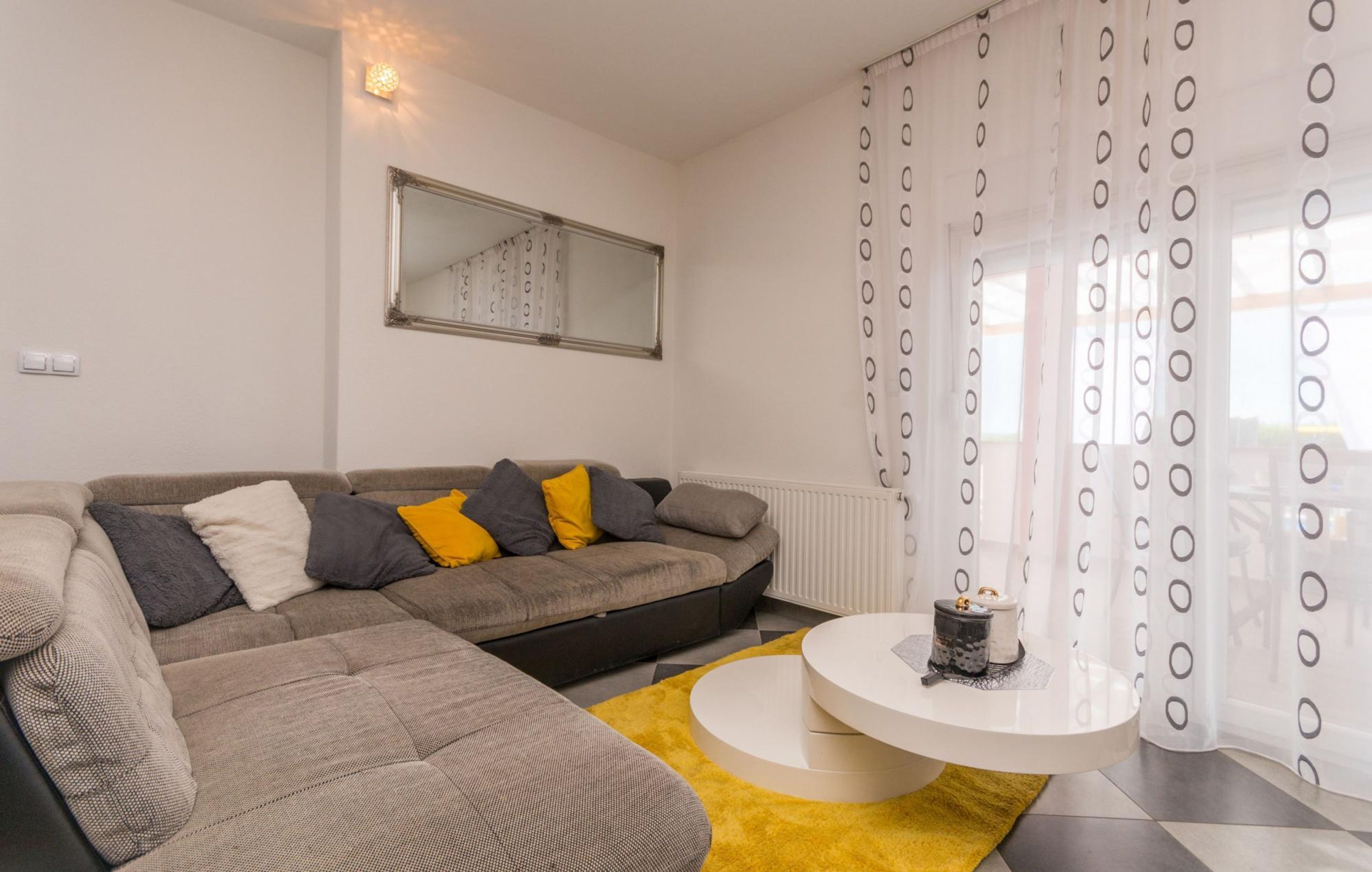 A modern living room with a sectional sofa, a round coffee table, and a large mirror on the wall.