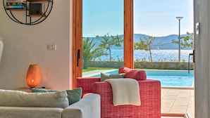 A modern living room with a red sofa, a grey sofa, and a floor lamp. A large window offers a view of a pool and a scenic landscape. - Villa Roberta Zadarvillas (Sveti Filip i Jakov)