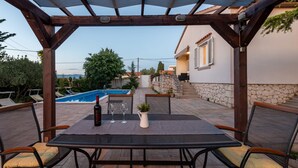 A covered outdoor seating area with a table, chairs, and a pool in the background. - Villa Me Trovi Zadarvillas (Zadar)