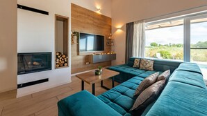 A modern living room with a large sectional sofa, a flat-screen TV, a fireplace, and a large window with a view of greenery. - Villa Descansa in Dracevac Ninski (Nin)