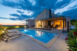 Ett modernt hus med en swimmingpool, utomhusmöbler och en täckt uteplats.