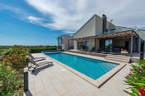 Ett modernt hus med en swimmingpool, utomhusmöbler och utsikt över landskapet.