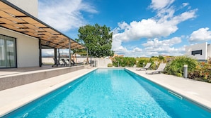 A rectangular swimming pool with clear blue water, surrounded by a concrete deck and a pergola with wooden slats. - Villa Descansa in Dracevac Ninski (Nin)