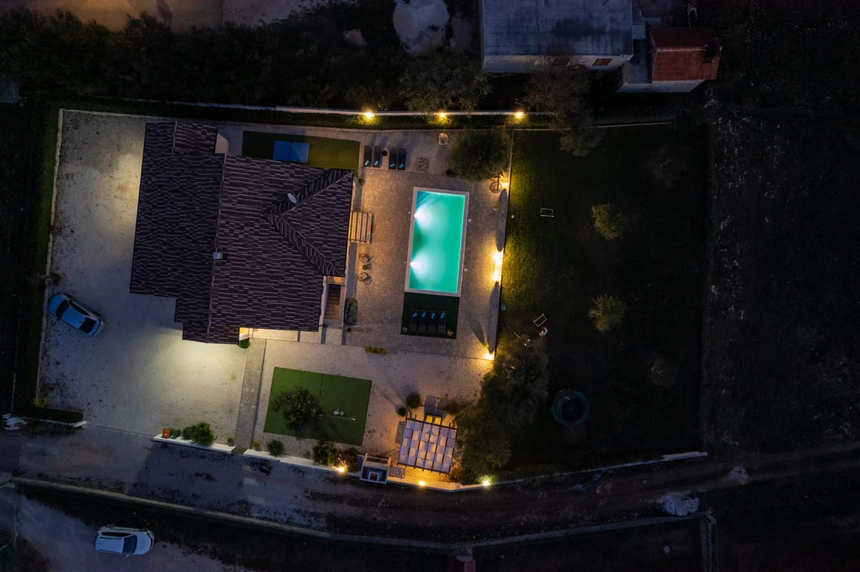 Luchtbeeld van een woonhuis met een zwembad, een overdekt terras en een oprit met geparkeerde auto's.