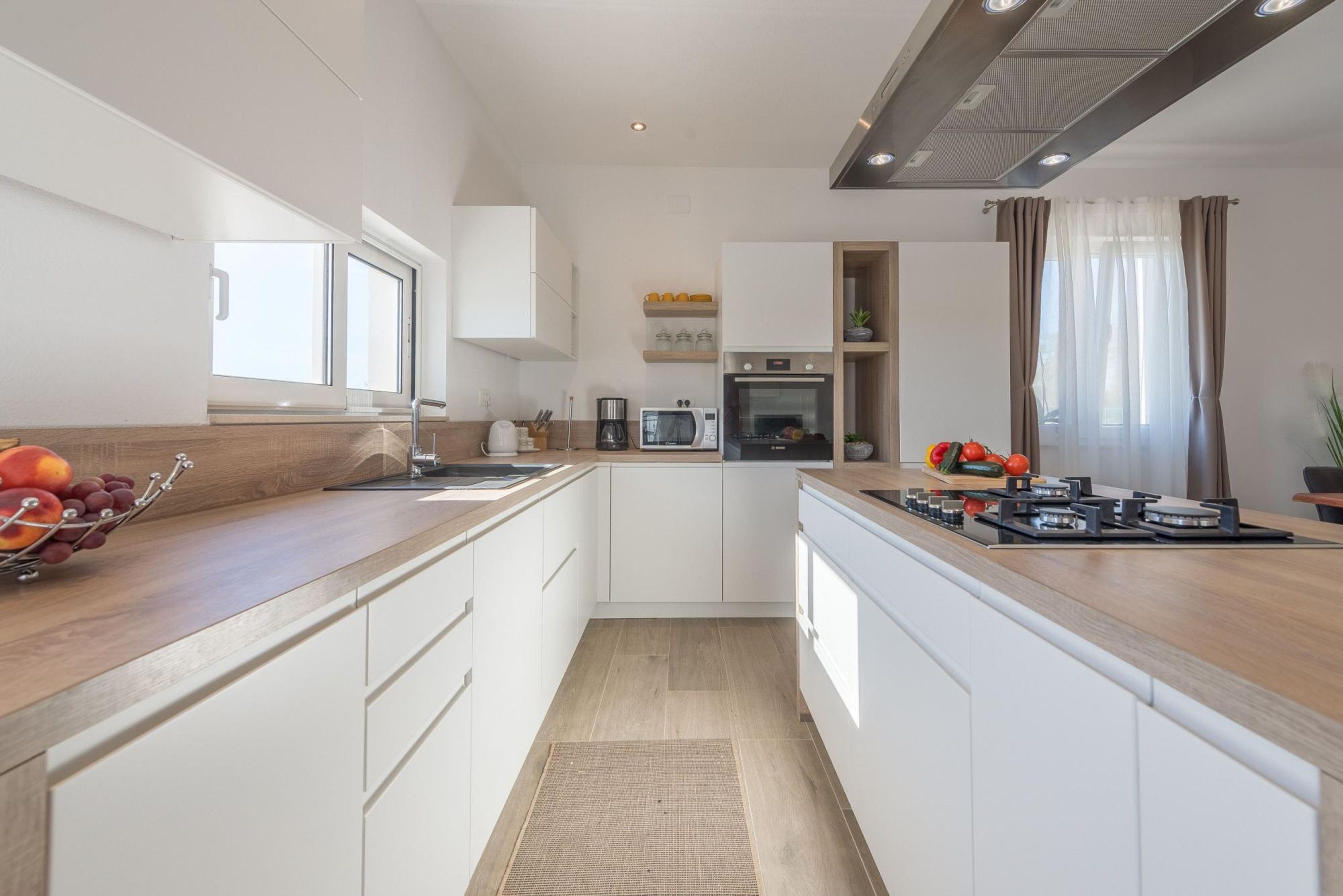 A modern kitchen with white cabinets, a wooden countertop, a built-in oven, and a gas stove.