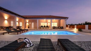 Un área de piscina moderna al aire libre con sillones de descanso, una zona de comedor y un patio bien iluminado.