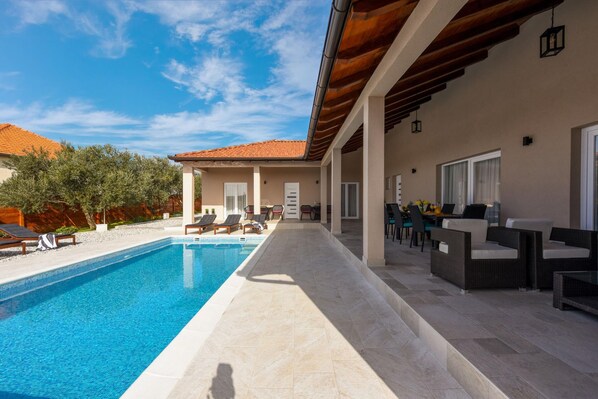 A swimming pool with lounge chairs, a covered patio area, and a dining setup.