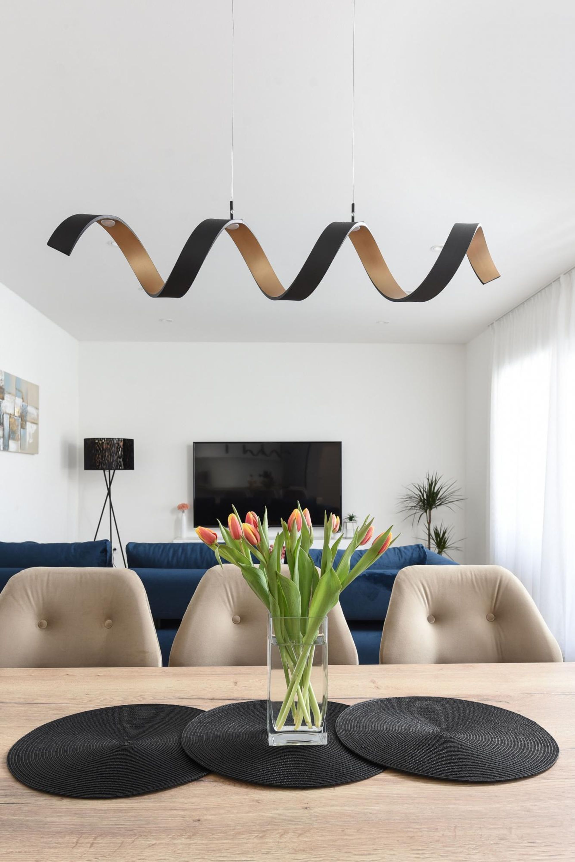Un salon moderne avec un canapé, une table basse ornée d’un vase de fleurs et un téléviseur fixé au mur.