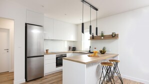 Una cocina moderna con armarios blancos, un refrigerador de acero inoxidable, una isla de madera con taburetes e iluminación colgante.