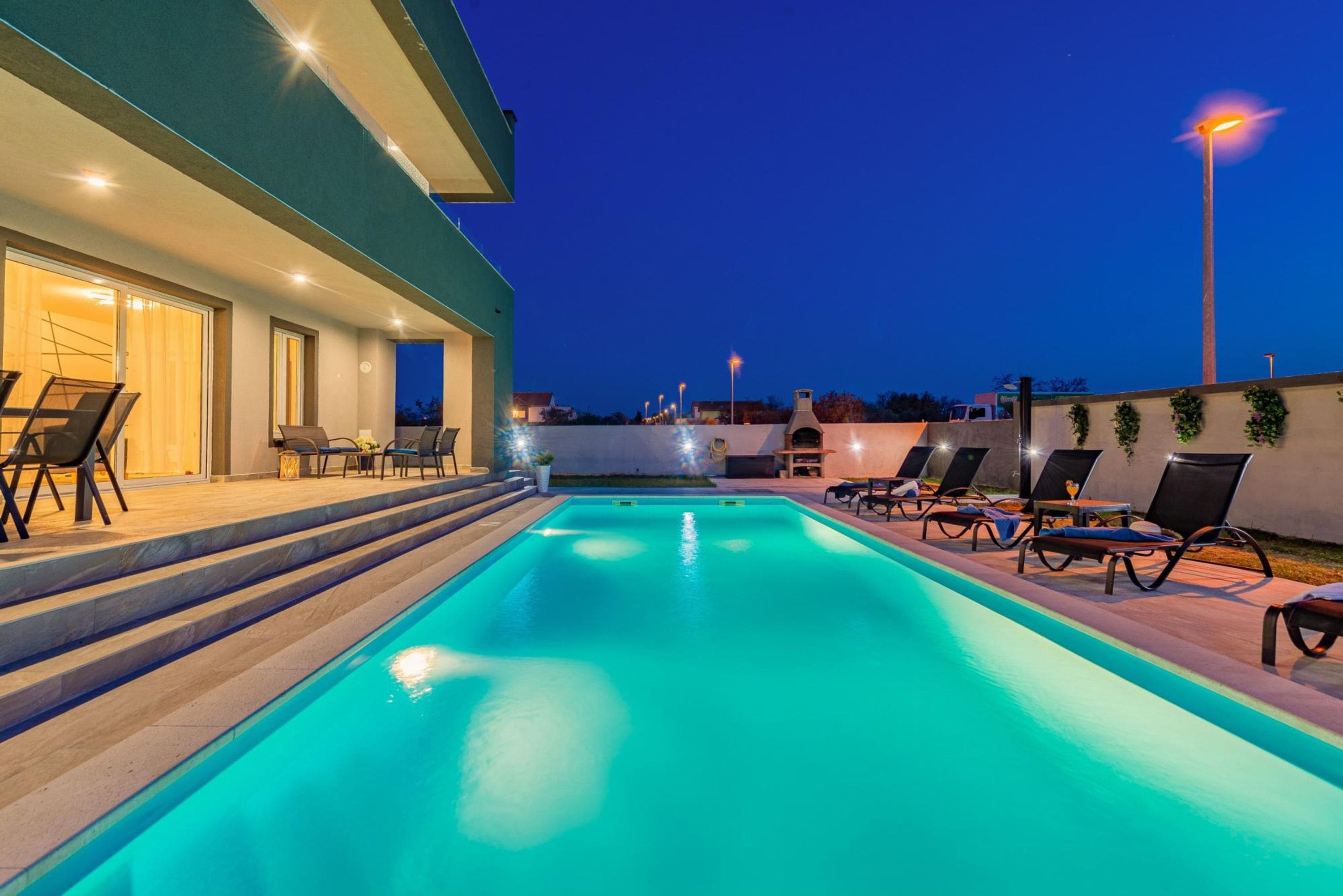 A swimming pool with lounge chairs and steps leading to a covered area with seating.