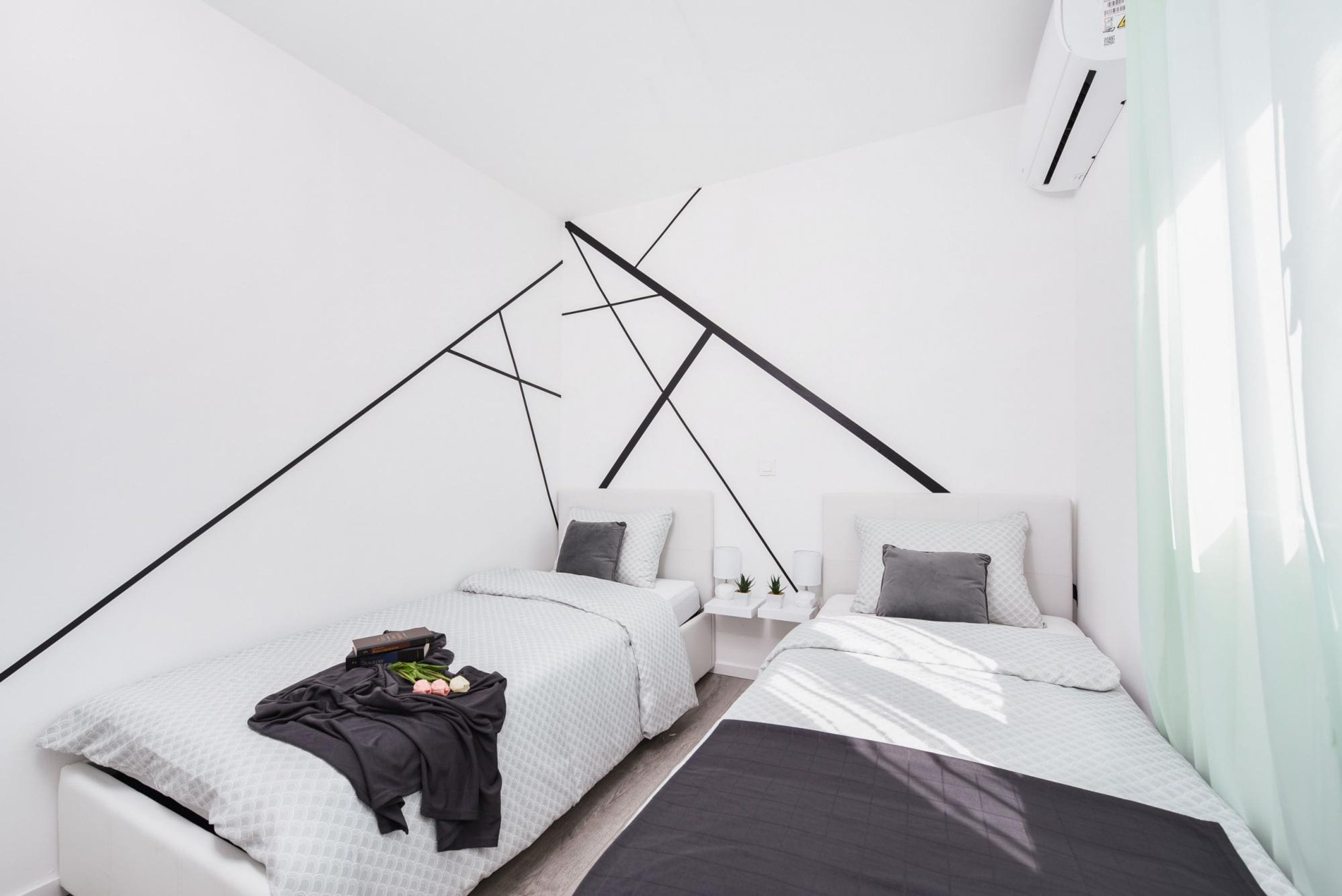 A modern bedroom with two beds, a white wall, and a slanted ceiling.