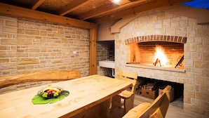 A stone fireplace with a fire, wooden beams, and a table with a fruit bowl. - Villa Kamen Zadarvillas (Novigrad)