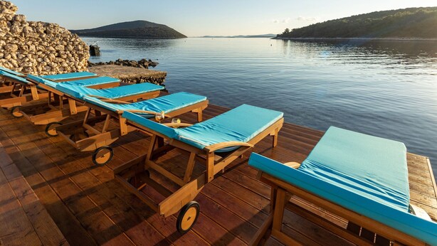 Una terraza de madera con sillones de descanso y un muro de piedra junto a un lago tranquilo.