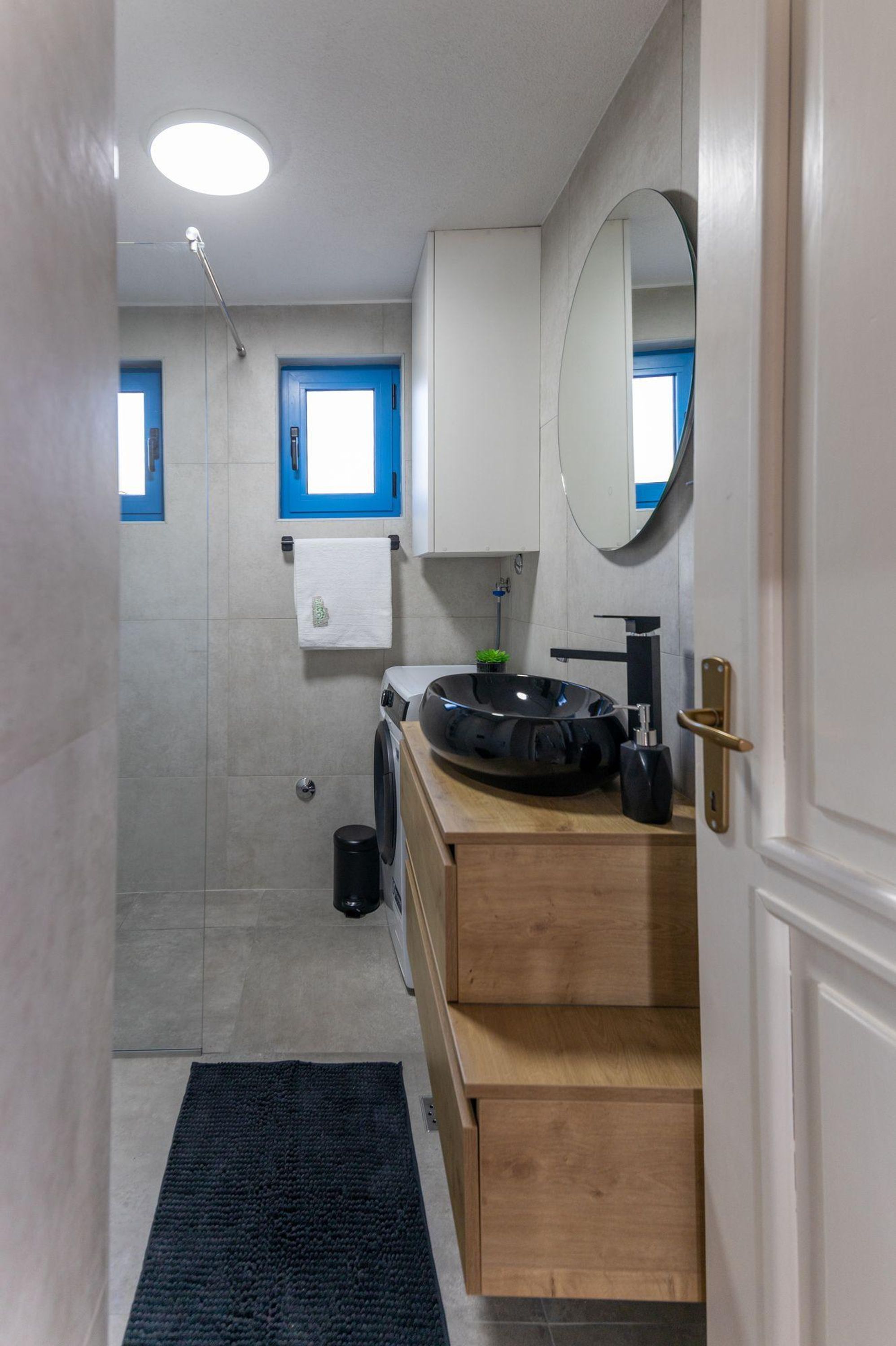 A modern bathroom with a wooden vanity, a black sink, and a mirror. There is a towel rack above the sink and a small plant on the counter.