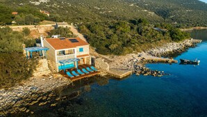 Una casa costera con fachada de piedra, techo de tejas rojas y un balcón con sillones de playa azules.