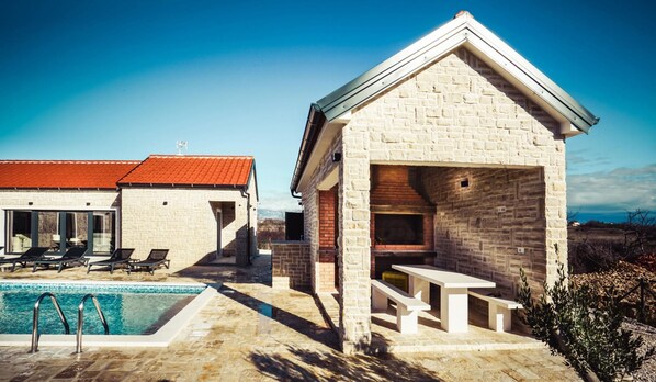 Un edificio de piedra con techo rojo, piscina y mobiliario exterior.