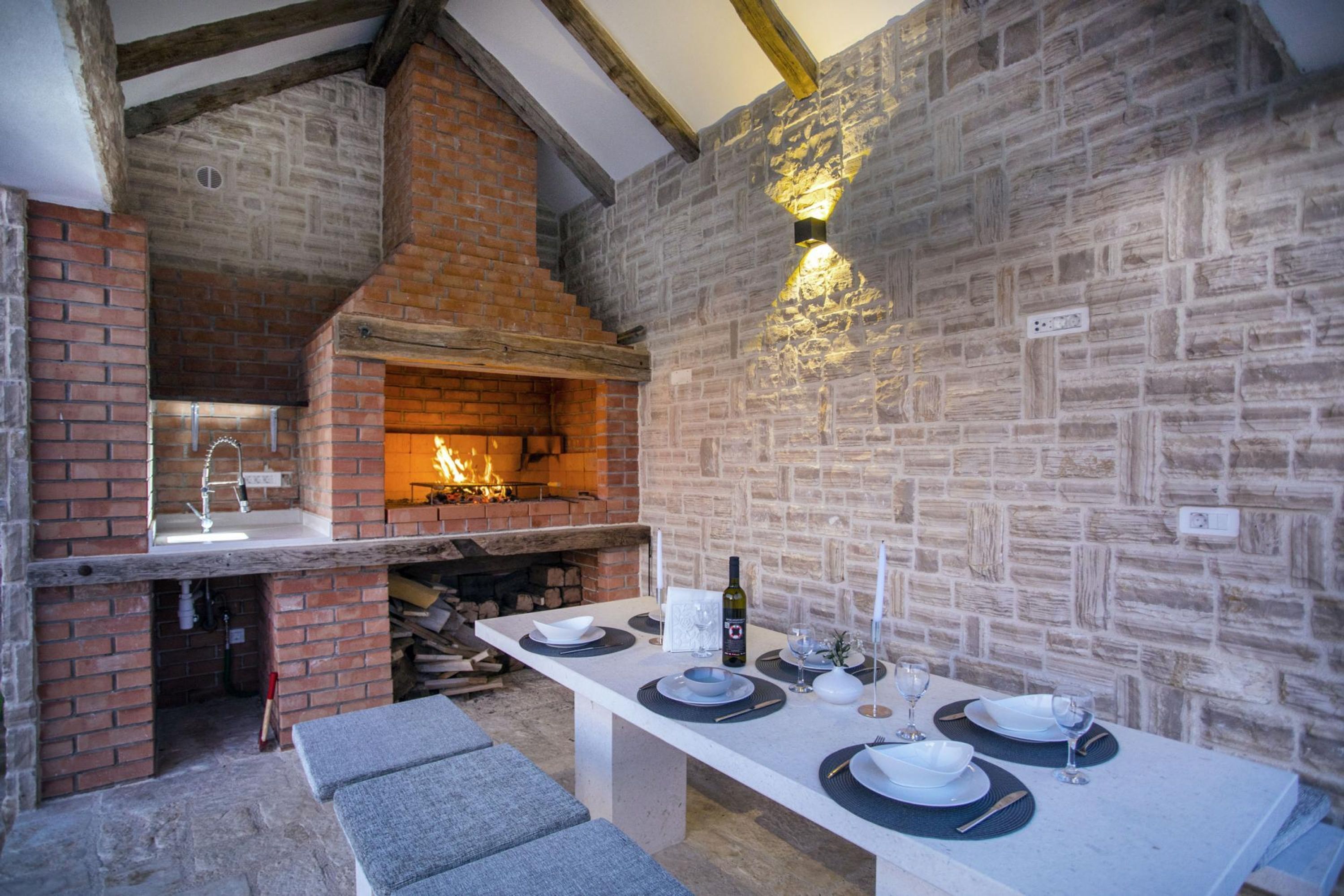 An outdoor dining area with a brick fireplace, stone walls, and a long table set for four.