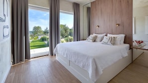 Une chambre moderne avec un grand lit, une tête de lit en bois et une vue sur un jardin, visible à travers une grande fenêtre.