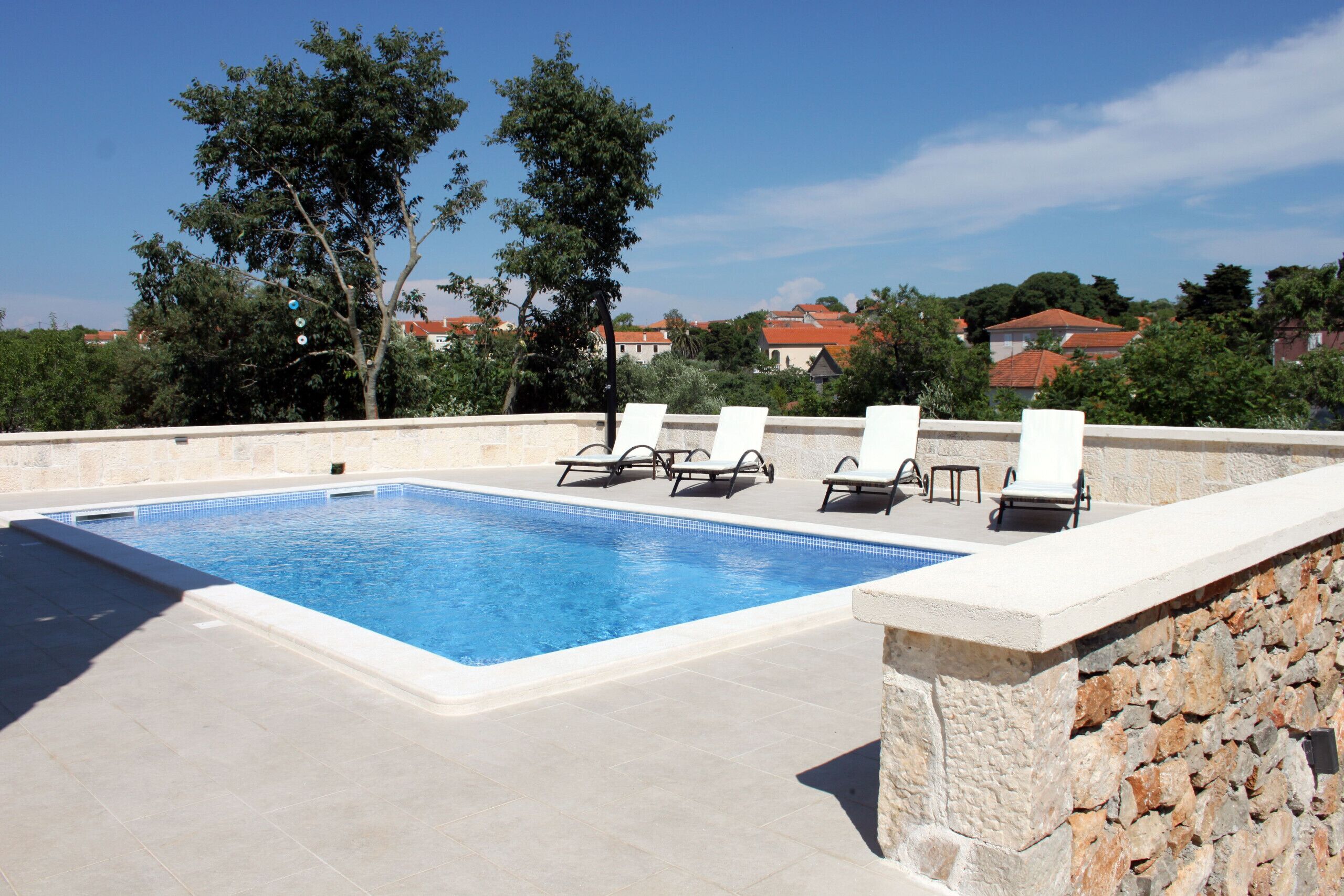 A rectangular swimming pool with a stone wall and lounge chairs.