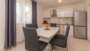 Una cocina moderna con armarios blancos, un refrigerador de acero inoxidable y una mesa de comedor con cuatro sillas.