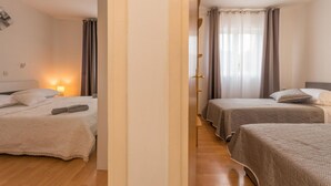 Habitación de hotel con dos camas, piso de madera, una mesita de noche con lámpara y una ventana con cortinas.